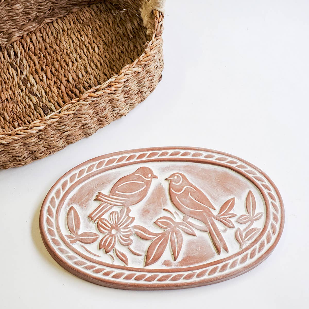 Terracotta bread warming  plate with lovebirds design next to a woven basket