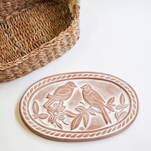 Terracotta bread warming  plate with lovebirds design next to a woven basket