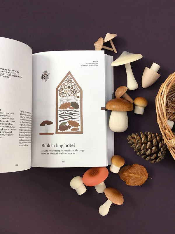 'The Nature of Play' book opened with illustrations of a bug hotel, surrounded by small mushrooms and a wicker basket on a dark background.